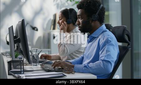 Collaborazione diversificata con il call center boss caucasico che spiega l'attività puntando il dito auricolare per operatore africano chiamata di lavoro al computer femminile indiano Foto Stock