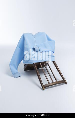 Felpa blu chiaro appesa su una sedia in legno rovesciata su sfondo chiaro. Foto verticale. Foto Stock