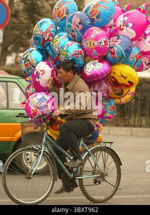 28 marzo 2006, PECHINO, CINA: Un uomo cinese batte con i suoi palloncini attraverso un vento rigido mentre cerca di vendere palloncini con personaggi dei cartoni animati statunitensi e giapponesi per le strade di Pechino, Cina, il 28 marzo 2006. Quest'anno la Cina affronterà sfide occupazionali "serie” e probabilmente creerà meno della metà dei posti di lavoro necessari per far fronte a eserciti in rapida crescita di nuovi in cerca di lavoro e licenziamenti di lavoratori, ha affermato in una pessima previsione il principale pianificatore economico del paese comunista. (Immagine di credito: © Stephen Shaver/ZUMA Press Wire) Foto Stock