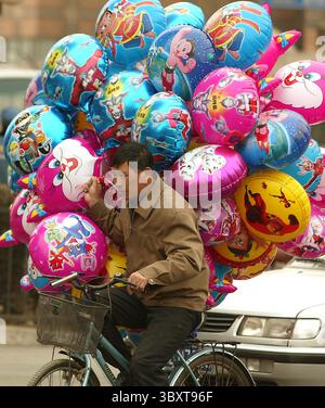 28 marzo 2006, PECHINO, CINA: Un uomo cinese batte con i suoi palloncini attraverso un vento rigido mentre cerca di vendere palloncini con personaggi dei cartoni animati statunitensi e giapponesi per le strade di Pechino, Cina, il 28 marzo 2006. Quest'anno la Cina affronterà sfide occupazionali "serie” e probabilmente creerà meno della metà dei posti di lavoro necessari per far fronte a eserciti in rapida crescita di nuovi in cerca di lavoro e licenziamenti di lavoratori, ha affermato in una pessima previsione il principale pianificatore economico del paese comunista. (Immagine di credito: © Stephen Shaver/ZUMA Press Wire) Foto Stock
