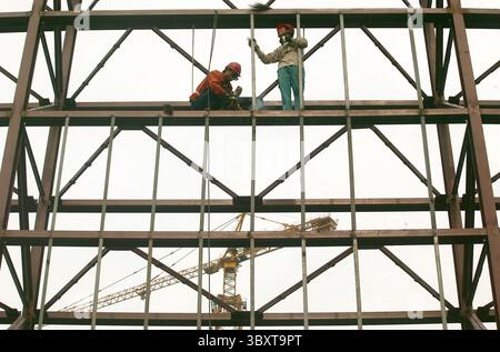2 agosto 2006, PECHINO, CINA: Gli operai edili cinesi assemblano impalcature in acciaio su una struttura olimpica nel centro di Pechino, 2 agosto 2006. I funzionari stanno esaminando nuovi passi per rinfrescare l'economia sfrigolante della Cina, mentre la sua principale agenzia di pianificazione ha chiesto un credito bancario più stretto e restrizioni sulla costruzione, hanno riferito i media statali. I rapporti di mercoledì hanno suggerito che Pechino ritiene che le misure precedenti, tra cui un aumento del tasso di interesse ad aprile, non stiano contenendo la crescita fuorviante della spesa per le fabbriche e altre risorse che i leader cinesi temono potrebbero innescare una crisi finanziaria. (Immagine di credito: © Stephe Foto Stock