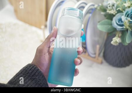 Tenere una bottiglia d'acqua traslucida in un ambiente accogliente Foto Stock