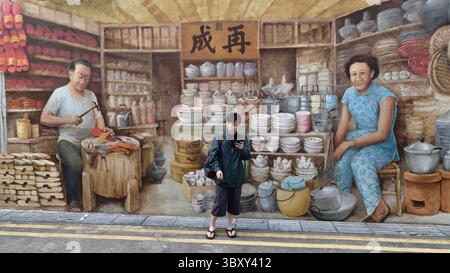 Un uomo cinese si trova di fronte a un murale a Chinatown, Singapore, raffigurante un vecchio negozio cinese di utensili per la casa e un calzolaio cinese Foto Stock