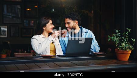 Laptop, brindisi e una coppia con un caffè al bar con risata, chiacchierare o parlare insieme la mattina. Felice, cappuccino e uomo con donna accesa Foto Stock