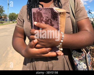 Primo piano di una donna africana che tiene una Bibbia logora stretta contro il petto, simboleggia la fede profonda, la devozione e la forza spirituale. Catturati Foto Stock