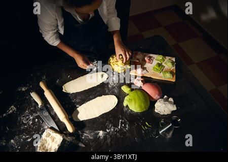 Uno chef che crea ravioli fatti in casa usando vibranti impasti rossi, verdi e bianchi su una superficie infarinata, mettendo in risalto l'arte culinaria italiana tradizionale e il cul Foto Stock