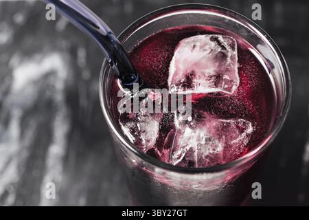 Bicchiere di bevanda rossa con cubetti di ghiaccio e paglia. Dettaglio rinfrescante delle bevande fredde su sfondo scuro. Cocktail per feste estive. Foto Stock