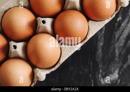 Uova di pollo marroni in cartone. Vista dall'alto delle uova fresche biologiche. Prodotto alimentare naturale. Contenitore delle uova di fattoria su pietra nera. Ingrediente salutare per la colazione. Foto Stock