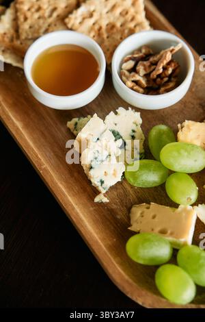 Un piatto di formaggi gourmet con formaggio blu, camembert, uva verde, noci e miele, elegantemente sistemato su una tavola di legno per un lussuoso culi Foto Stock
