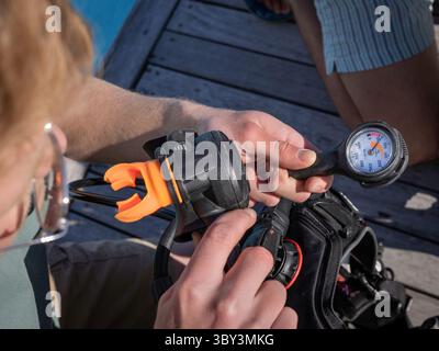 Primo piano dell'immersione con le mani che tengono il regolatore e controllano il manometro. Foto Stock