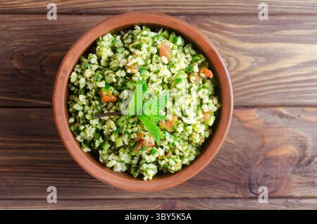 Tabbouleh con insalata orientale in una ciotola di ceramica su un tavolo di legno. Concetto di cucina tradizionale libanese o siriana. Piatti vegetariani o vegani. F. Selettiva Foto Stock