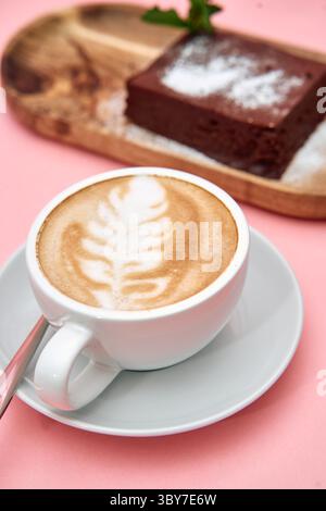 Un latte cremoso con delicata foglia d'arte e una torta al cioccolato decadente, splendidamente presentata su una superficie rosa, crea un'atmosfera accattivante e accattivante Foto Stock