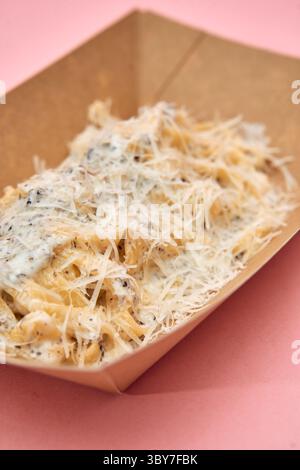 Una porzione di tagliatelle cremose ricoperte di salsa al tartufo e condite con parmigiano grattugiato, elegantemente presentate in un contenitore ecologico contro a pi Foto Stock