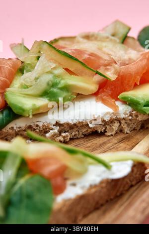 Un appetitoso panino a vista con avocado cremoso, salmone affumicato e formaggio spalmabile su pane rustico integrale, perfetto per un pasto nutriente Foto Stock