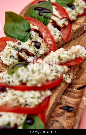 Una bruschetta preparata al momento con ricotta cremosa, pomodori succosi, foglie di basilico e un filo balsamico sul pane rustico, che mostra un vivace e g Foto Stock