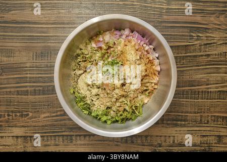 Vista dall'alto di una ciotola con erbe tritate, cipolle tagliate a dadini e varie spezie aggiunte alla carne macinata Foto Stock