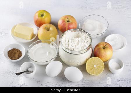 Alimenti, ingredienti per cheesecake fatti in casa o torta di mele: Mele, farina, panna acida o yogurt, burro, zucchero, uova, lievito in polvere, limone, cannella e. Foto Stock