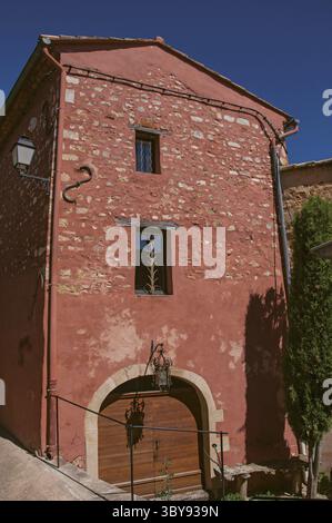 Vista della tradizionale casa colorata in ocra sotto un cielo azzurro soleggiato, nel centro della città del villaggio di Roussillon. Situato nel dipartimento di Vaucluse Foto Stock