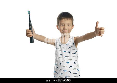 Un ragazzo con una camicia di dinosauro che regge uno spazzolino da denti dà un pollice in su - un sorriso sano! Sfondo bianco Foto Stock