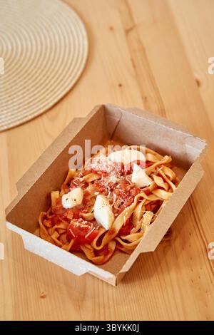 Scatola ecologica contenente deliziose tagliatelle ricoperte di pomodori freschi e mozzarella, per una delizia culinaria tradizionale. Foto Stock