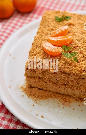 Una torta al miele a strati con un condimento sbriciolato è elegantemente guarnita con fette di mandarino su un piatto bianco, offrendo un ricco e appagante piatto da dessert Foto Stock