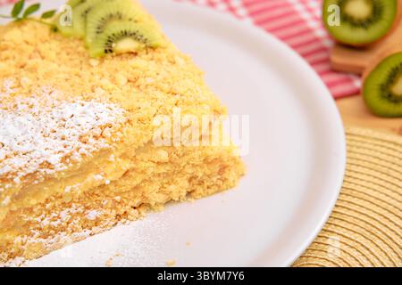 Questa immagine mostra una torta sbriciolata al limone con fette di kiwi sulla parte superiore, spolverata con zucchero a velo e servita su un piatto bianco, catturando un appea fresco Foto Stock