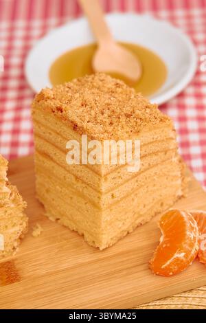 Una deliziosa torta al miele a strati con un condimento di briciole si trova su una tavola di legno, accompagnata da fette di mandarino fresche, pronte a deliziare le papille gustative. Foto Stock