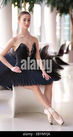 Elegante ballerina in tutu nero seduta graziosamente su sedia bianca all'interno Foto Stock