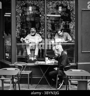 Due uomini leggono tranquillamente all'interno di un caffè di Bristol, mentre una terza persona siede all'esterno, sorseggiando un drink a un tavolino. L'atmosfera e' calma e intima, perf Foto Stock