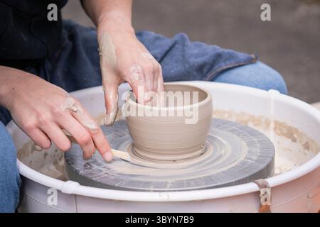 Primo piano di vaschette per preparare le mani. La donna ha cullato le mani intorno all'argilla bagnata su una ruota di vasai. Donna che produce ceramiche in un laboratorio di ceramica. Foto Stock