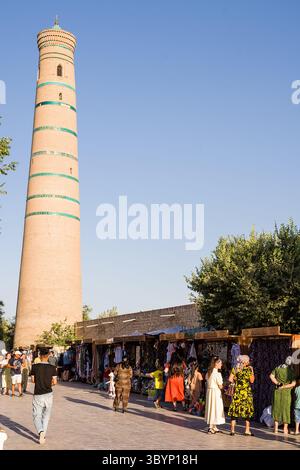 Khiva, Uzbekistan - 12 luglio 2024: Minareto di Djuma visto dalla strada del mercato con bancarelle e venditori, Khiva, Uzbekistan Foto Stock