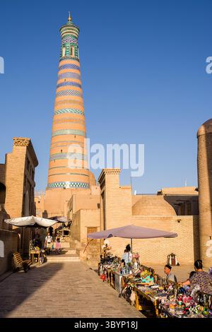 Khiva, Uzbekistan - 12 luglio 2024: Minareto di Khodja visto dalla strada con bancarelle e venditori locali, Khiva, Uzbekistan Foto Stock