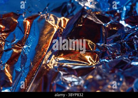 Uno scatto ravvicinato di lamina di alluminio arricciata, che riflette un mix di luce blu e arancione. I motivi astratti e le trame creano un aspetto visivamente interessante Foto Stock