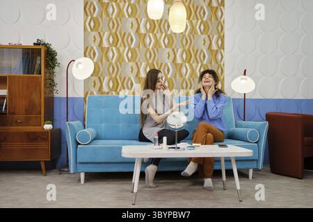 In un salotto elegante, due donne condividono un momento di gioia mentre si prendono cura della pelle dei loro volti Foto Stock
