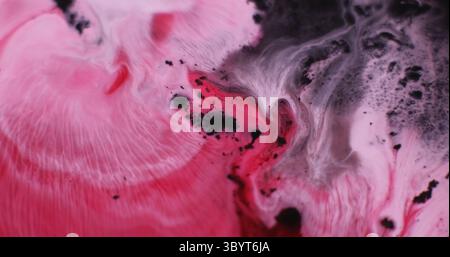 Spandimento della vernice. Mix di colori. Macchie ondulate fluide con emulsione d'acqua cremisi rosa defocalizzate su sfondo nero scuro con grafica astratta. Foto Stock