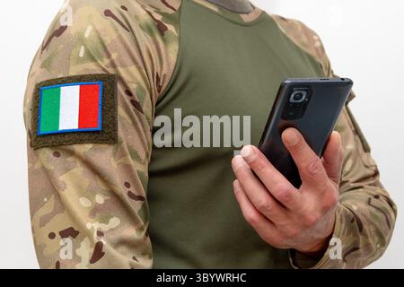 Un uomo in uniforme militare con la bandiera italiana che tiene un cellulare Foto Stock