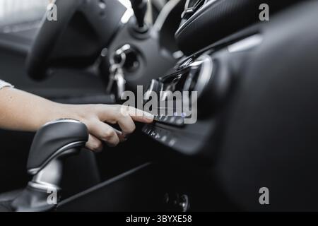 Giovane donna che regola la climatizzazione della vettura con climatizzatore o centralina del sistema climatico. Vista interna di un'auto. Concetto di utente e auto Foto Stock
