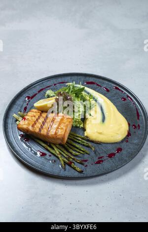 Il filetto di salmone grigliato viene servito su un letto di asparagi con un lato di purè di patate e un cuneo di limone Foto Stock