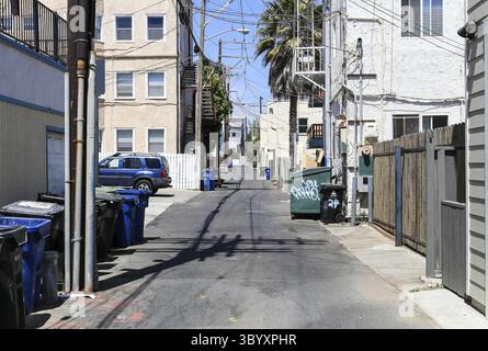 Una tipica strada secondaria con i bidoni della spazzatura in piedi sul lato e un'auto parcheggiata. Anche i pali di alimentazione si trovano sul ciglio della strada, Los Angeles, Stati Uniti Foto Stock