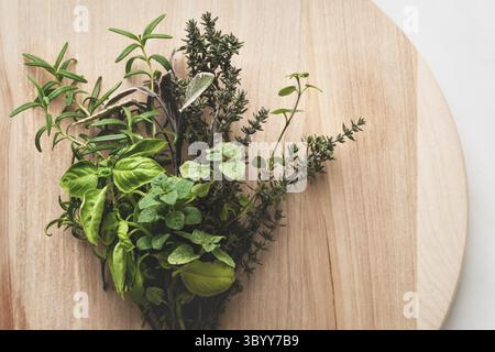 Pacchetto di erbe mediterranee italiane per cucinare su un tondo tagliere di legno Foto Stock