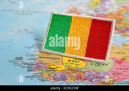 Bandiera Mali ecologica ricamata con filo e tessuto, collocata su una mappa del mondo che evidenzia il Mali nell'Africa occidentale. Concetto di viaggio e sostenibilità. Foto Stock