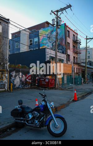 Una motocicletta Harley Davidson lungo una strada secondaria a East Vancouver con un murale su un edificio alle spalle. Foto Stock