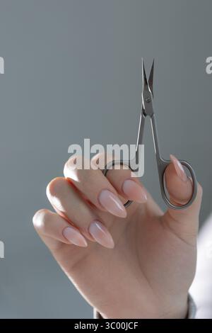 Forbici da maestro di manicure in mano, con una perfetta manicure beige in primo piano nel salone Foto Stock