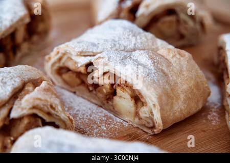 Primo piano di strudel di mele a fette su una tavola di legno, che mostra la sua crosta scrosciante, dorata e il ripieno di mele speziate alla cannella spolverato di zucchero a velo. Foto Stock