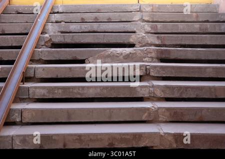 Vecchie scale in cemento in un sottopassaggio, usurate e riparate grossolanamente. Due guide metalliche arrugginite fungono da rampa improvvisata, mostrando segni di decadimento e avvicinamento Foto Stock