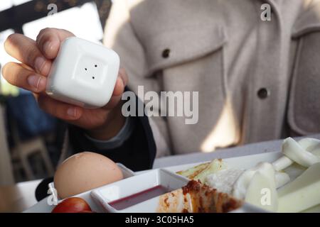 Tenere a mano uno shaker di sale sopra un piatto per la colazione Foto Stock