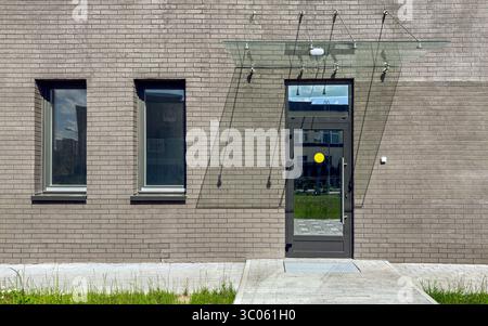 facciata di un moderno edificio di appartamenti. sfondo murato grigio con porta e due finestre. Foto Stock
