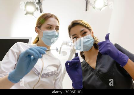 Dal basso dentisti con specchio e dispositivo piegato sopra la paziente durante l'appuntamento in clinica odontoiatrica. Foto Stock