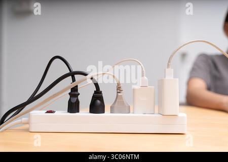 Primo piano della presa multipla con prese multiple e cavi aggrovigliati su una scrivania in legno. Concetto di elettricità, fornitura di energia, connessione di alimentazione, sicurezza e mo Foto Stock