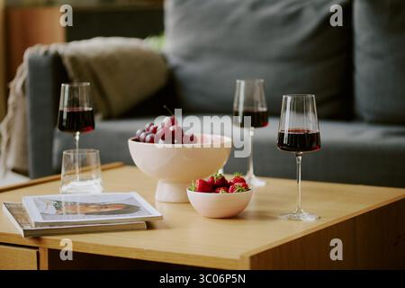 Bicchieri da vino rosso con uva fresca e fragole su tavolino da caffè in legno Foto Stock